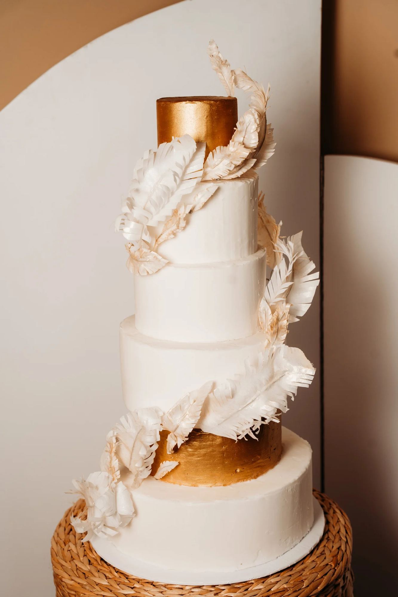 Tiered white wedding cake with gold and feather details